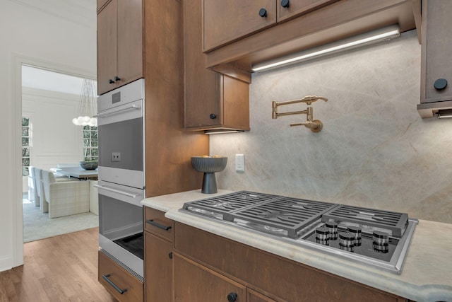 kitchen featuring tasteful backsplash, brown cabinetry, wood finished floors, stainless steel appliances, and light countertops