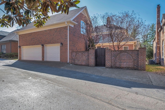 view of side of home featuring driveway, a garage, a gate, cooling unit, and brick siding