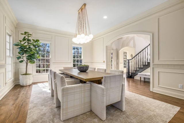 dining space featuring an inviting chandelier, a decorative wall, crown molding, and wood finished floors