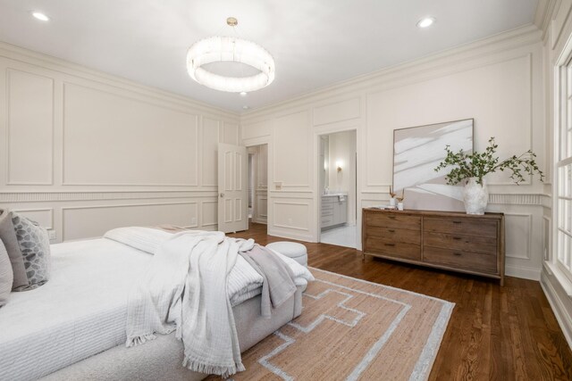 bedroom featuring connected bathroom, dark wood-style floors, ornamental molding, a decorative wall, and recessed lighting