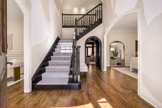 foyer entrance with arched walkways, a high ceiling, wood finished floors, and a decorative wall