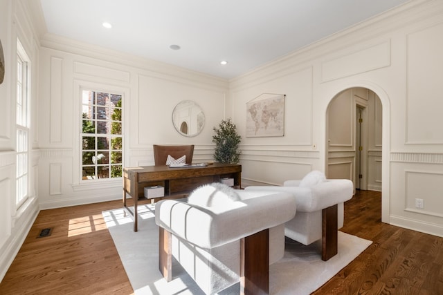 home office with arched walkways, crown molding, visible vents, a decorative wall, and wood finished floors