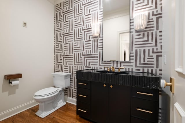 half bath featuring toilet, an accent wall, vanity, wood finished floors, and baseboards