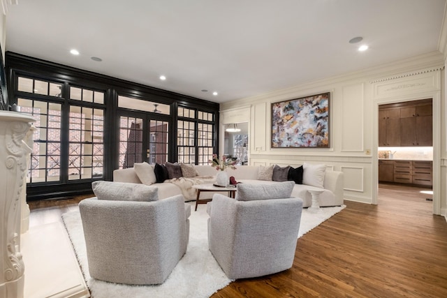 living area featuring ornamental molding, a decorative wall, wood finished floors, and recessed lighting