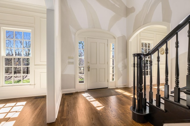 foyer entrance featuring arched walkways, wood finished floors, visible vents, baseboards, and stairway