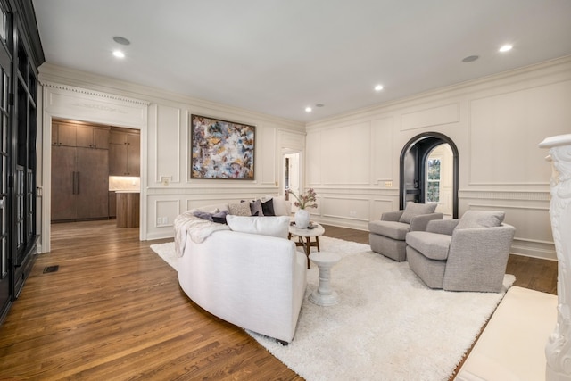 living area featuring arched walkways, a decorative wall, and wood finished floors