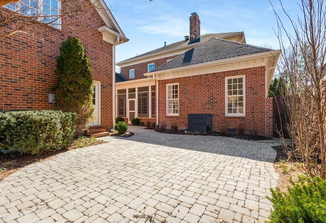 rear view of property with roof with shingles, brick siding, crawl space, and a chimney