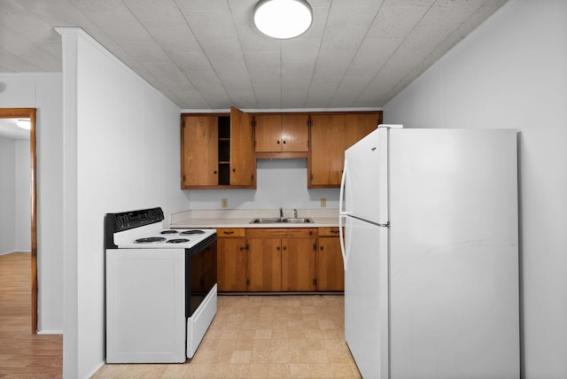 kitchen with electric range, a sink, light countertops, freestanding refrigerator, and brown cabinets