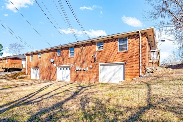 rear view of house featuring brick siding, a lawn, and an attached garage