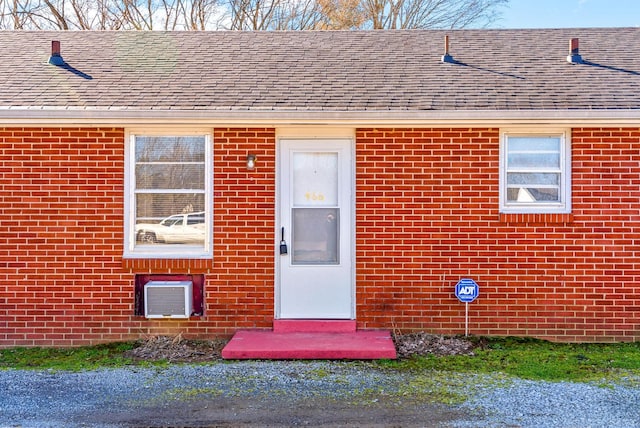 view of exterior entry with brick siding and roof with shingles