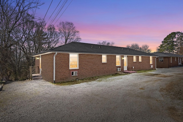 back of property at dusk featuring gravel driveway and brick siding