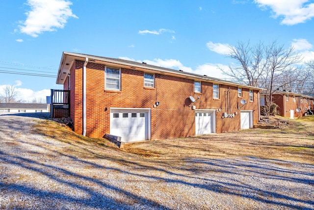 back of house with driveway, brick siding, and an attached garage