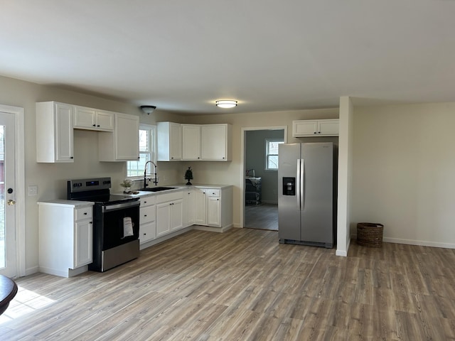 kitchen featuring light wood-type flooring, appliances with stainless steel finishes, white cabinets, and a sink