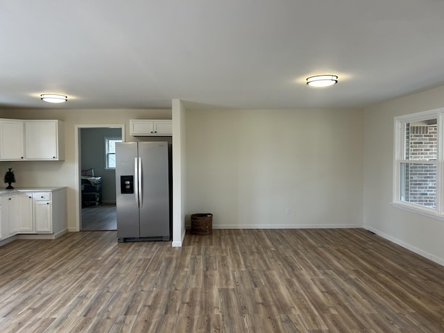 kitchen with wood finished floors, baseboards, white cabinets, light countertops, and stainless steel fridge