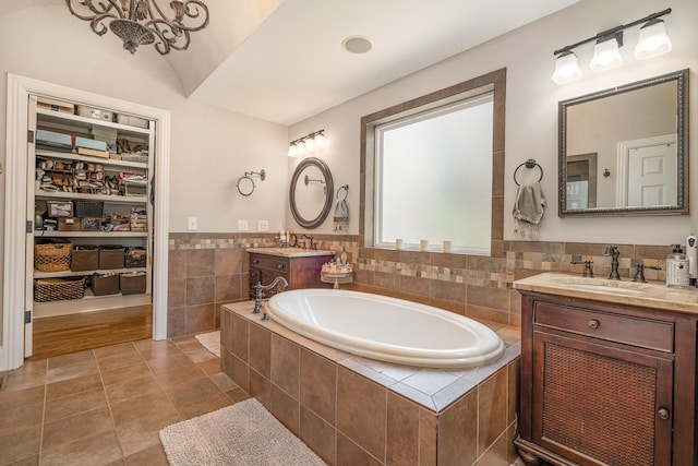 full bath with two vanities, a sink, a garden tub, tile patterned flooring, and tile walls