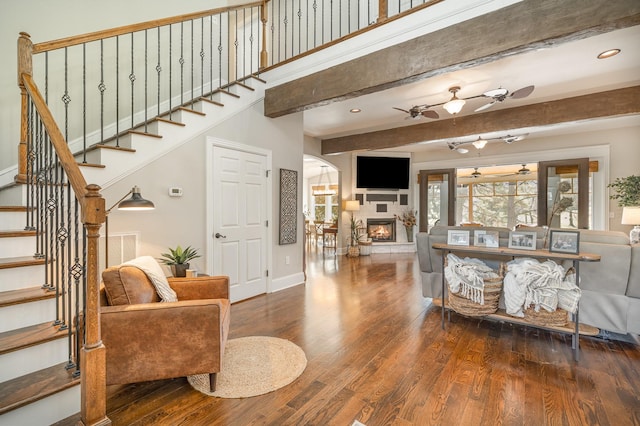 living area with a warm lit fireplace, stairway, beamed ceiling, and wood finished floors