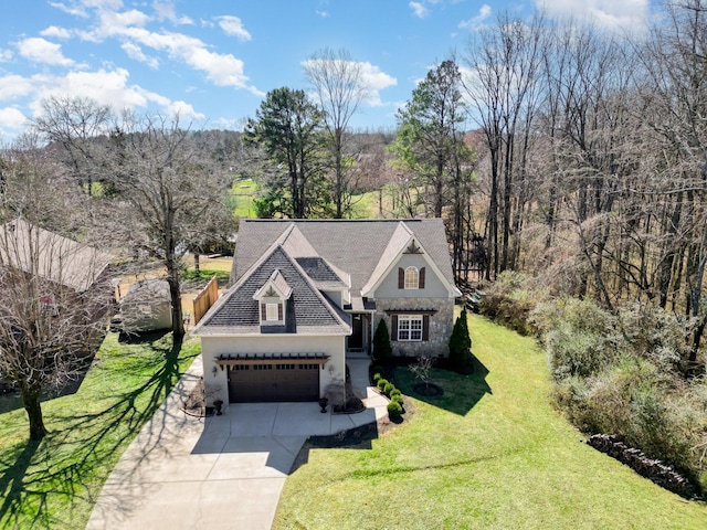 view of front of house with driveway, a garage, stone siding, a wooded view, and a front yard