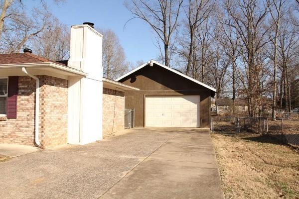 view of side of property featuring brick siding, a chimney, an attached garage, fence, and driveway