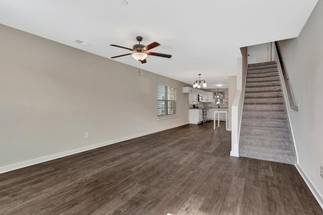 unfurnished living room with stairs, ceiling fan with notable chandelier, dark wood-style floors, and visible vents