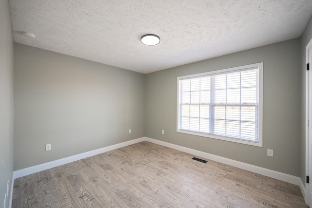 spare room with baseboards, visible vents, a textured ceiling, and light wood finished floors