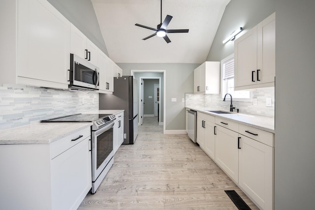 kitchen featuring lofted ceiling, a sink, white cabinetry, appliances with stainless steel finishes, and light wood-type flooring