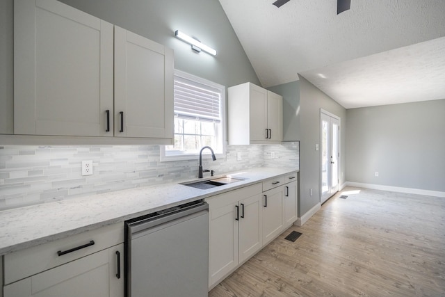 kitchen featuring white cabinets, lofted ceiling, dishwashing machine, a sink, and backsplash