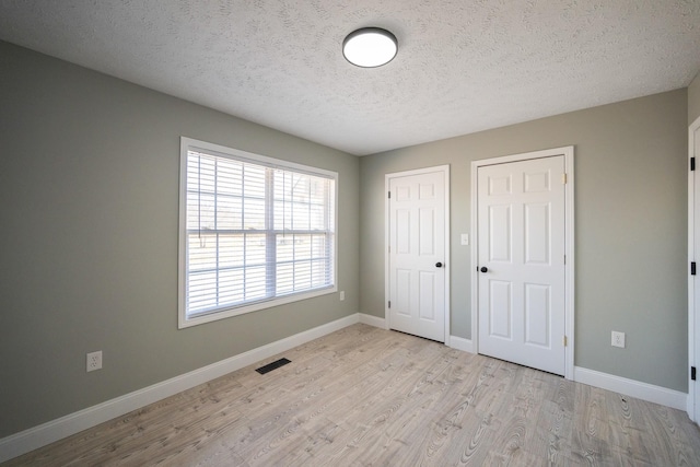 unfurnished bedroom featuring baseboards, visible vents, a textured ceiling, light wood-type flooring, and multiple closets