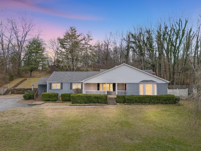 view of front of property featuring a porch, brick siding, a yard, and fence