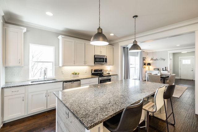 kitchen featuring stainless steel appliances, tasteful backsplash, ornamental molding, a kitchen island, and a sink