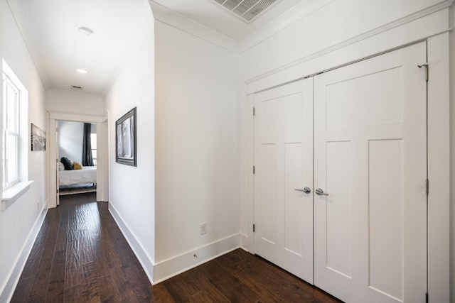 hallway with dark wood-style floors, visible vents, baseboards, and ornamental molding