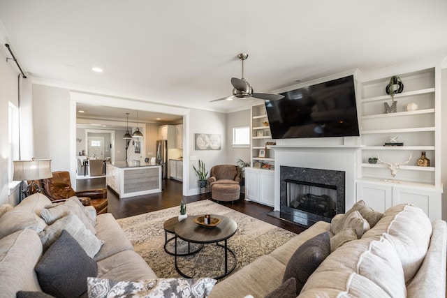 living room with dark wood-style floors, ceiling fan, a fireplace, and crown molding