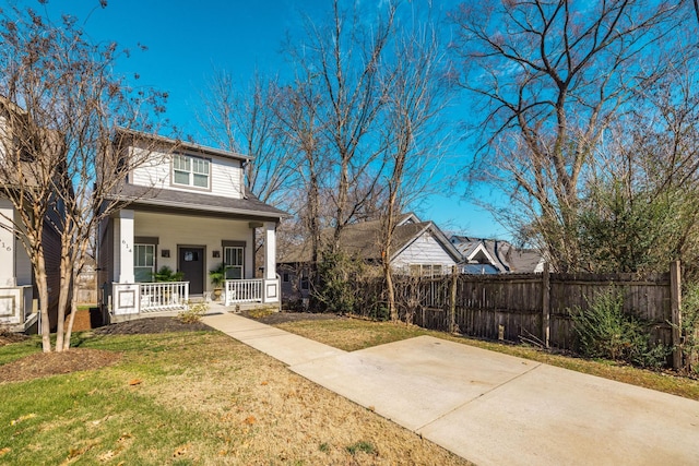 view of front of property featuring covered porch, fence, and a front lawn