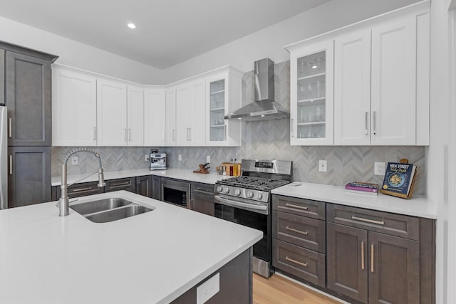 kitchen featuring a sink, light countertops, backsplash, wall chimney exhaust hood, and gas stove