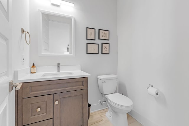 half bath with toilet, baseboards, wood finished floors, and vanity