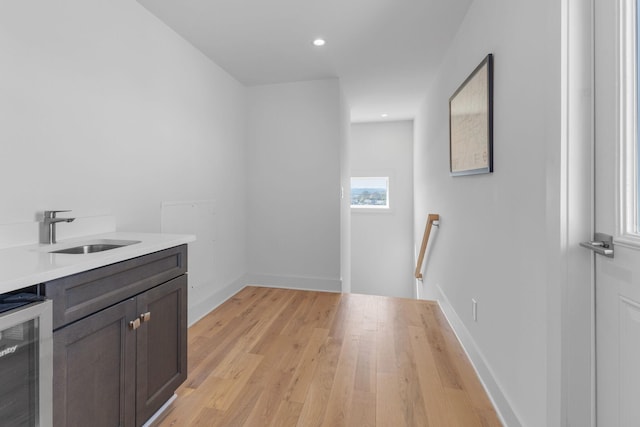 interior space with baseboards, wine cooler, light wood-type flooring, a sink, and recessed lighting