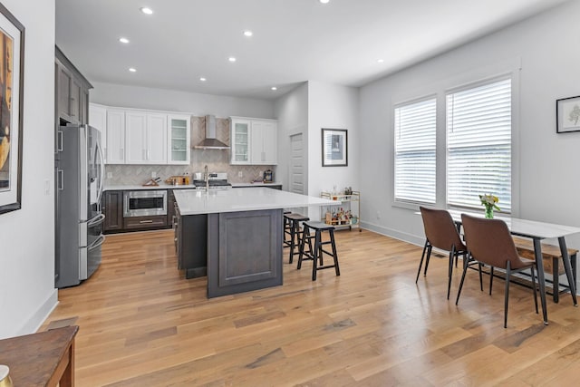 kitchen featuring stainless steel appliances, light countertops, decorative backsplash, light wood-style floors, and wall chimney range hood