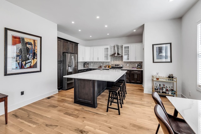 kitchen with stainless steel appliances, a kitchen breakfast bar, wall chimney range hood, backsplash, and light wood finished floors