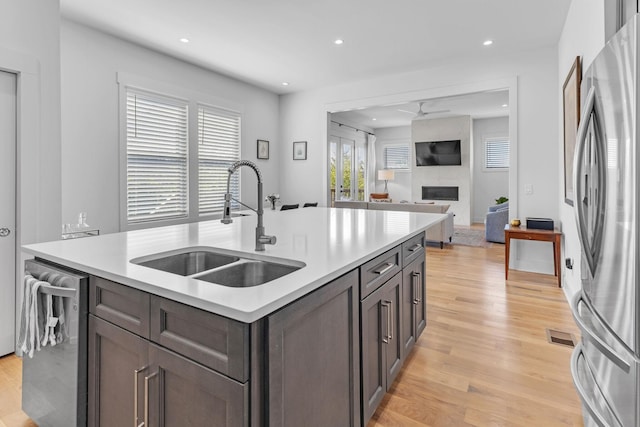 kitchen with stainless steel appliances, light countertops, light wood-style flooring, a high end fireplace, and a sink