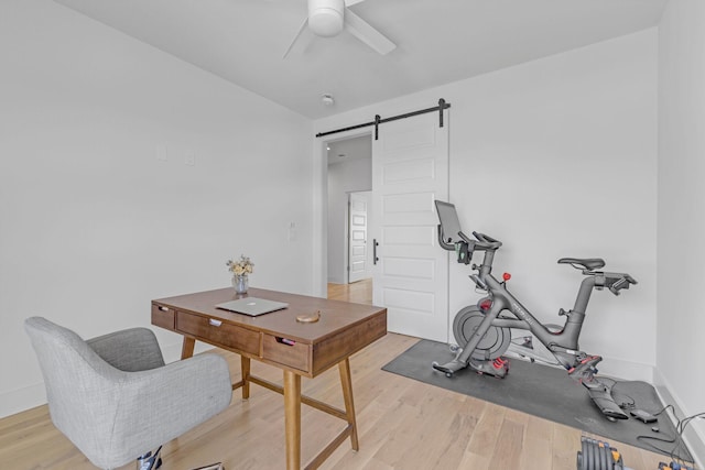 office space featuring baseboards, ceiling fan, light wood finished floors, and a barn door