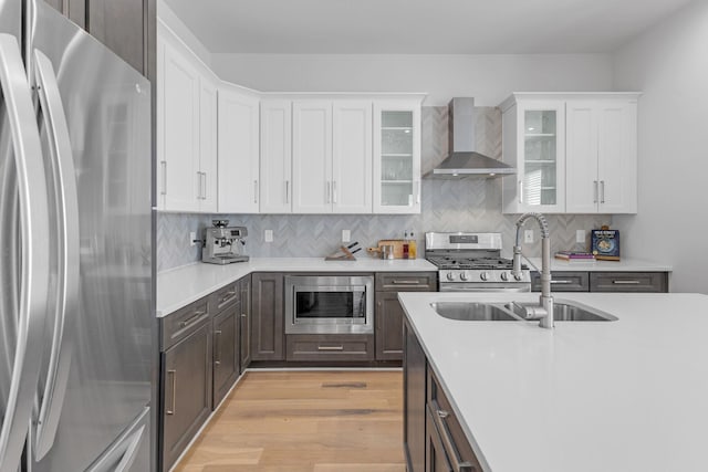 kitchen featuring light wood-style flooring, white cabinets, light countertops, appliances with stainless steel finishes, and wall chimney range hood