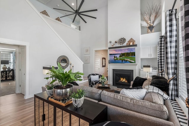 living room featuring a warm lit fireplace, a high ceiling, and wood finished floors