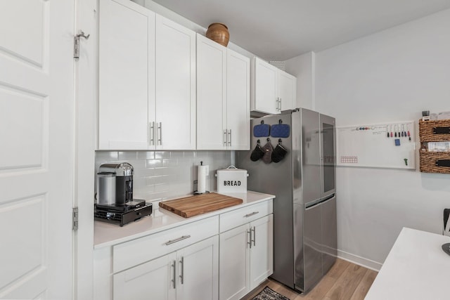 kitchen with white cabinets, light wood-style flooring, freestanding refrigerator, light countertops, and backsplash