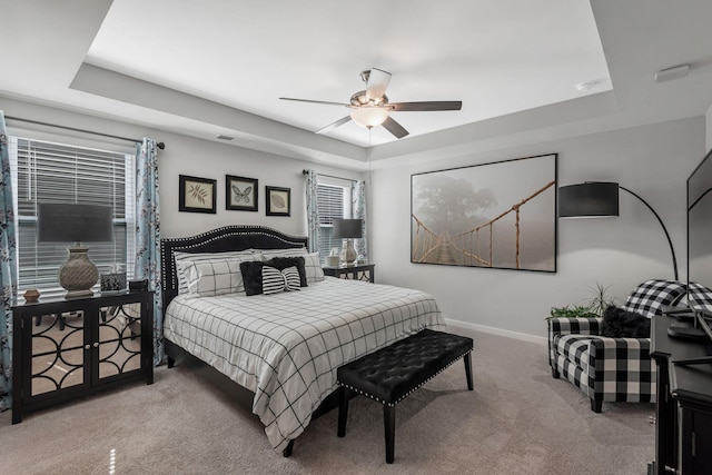 carpeted bedroom featuring ceiling fan, a tray ceiling, and baseboards