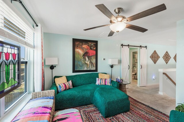 living area featuring carpet flooring, ceiling fan, baseboards, and a barn door