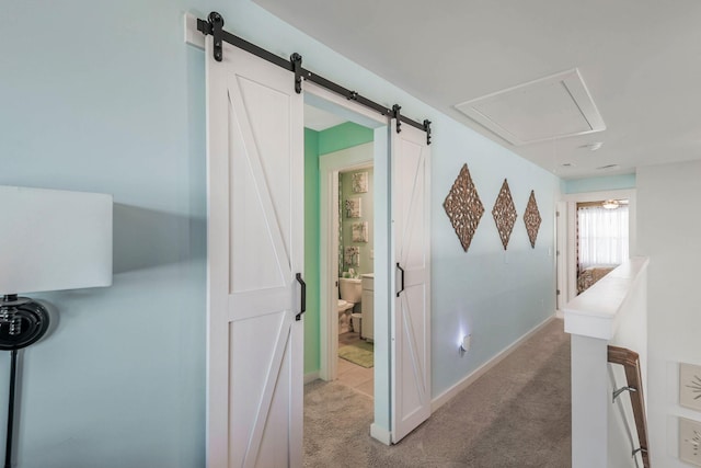 hall featuring light carpet, a barn door, attic access, baseboards, and an upstairs landing