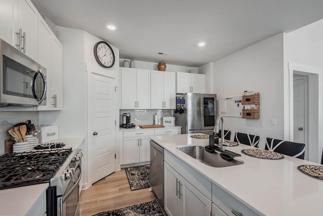 kitchen featuring white cabinets, appliances with stainless steel finishes, light countertops, light wood-style floors, and a sink