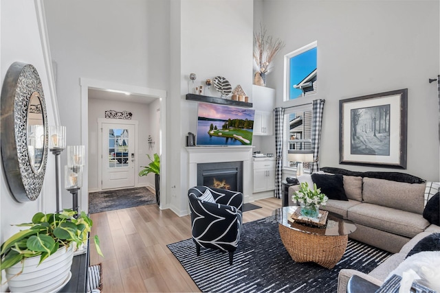 living room with baseboards, a glass covered fireplace, a towering ceiling, and light wood-style floors