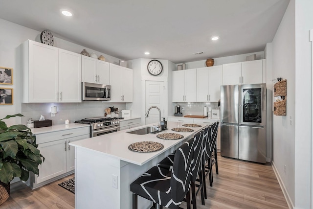 kitchen with light wood finished floors, a center island with sink, appliances with stainless steel finishes, a kitchen breakfast bar, and a sink