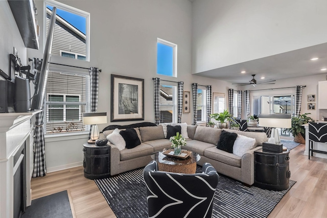 living area featuring light wood-type flooring, a towering ceiling, and baseboards