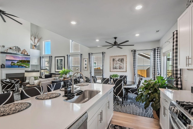 kitchen with appliances with stainless steel finishes, a ceiling fan, open floor plan, a sink, and a warm lit fireplace